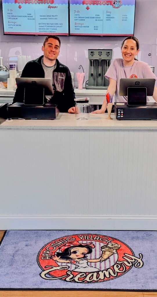 Two people stand behind cash registers at an ice cream shop.