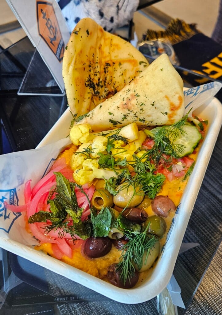 A colorful bowl featuring olives, onions and pita bread on hummus.