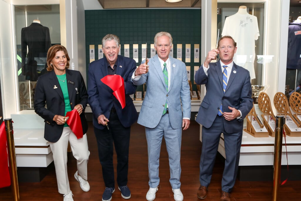 One women and three men cut a red ribbon in front of a museum.
