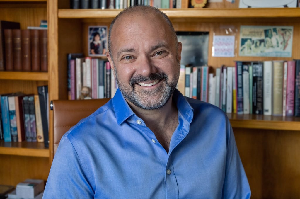 A man in a blue shirt in front of a bookcase.
