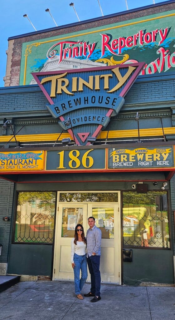 A couple stands in front of a pub on a sunny day.