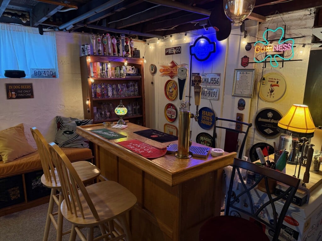 A basement home bar featuring wooden high top chairs, neon signs and quirky decor.
