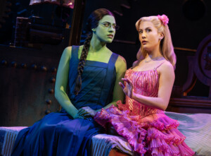 A green-skinned actress dressed in black beside a pale-skinned actress wearing a hot pink dress.