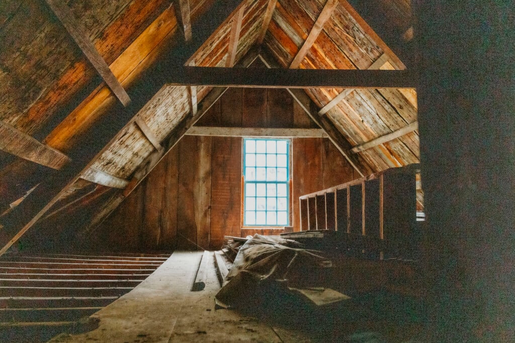 Sunlight floods an empty attic space from a lattice window.