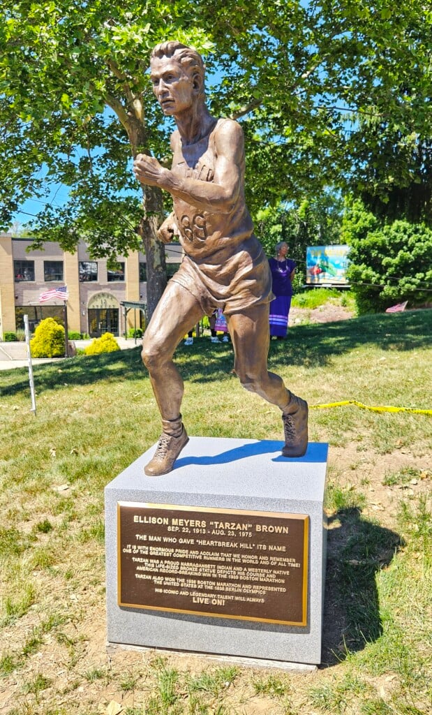 A brown statue of a man running is set against the backdrop of a park.
