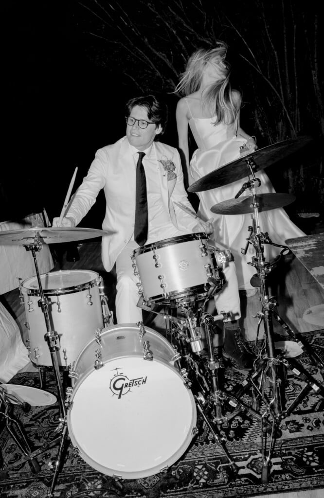 A black and white photo of a man playing a drum set and a woman dancing in a white dress.