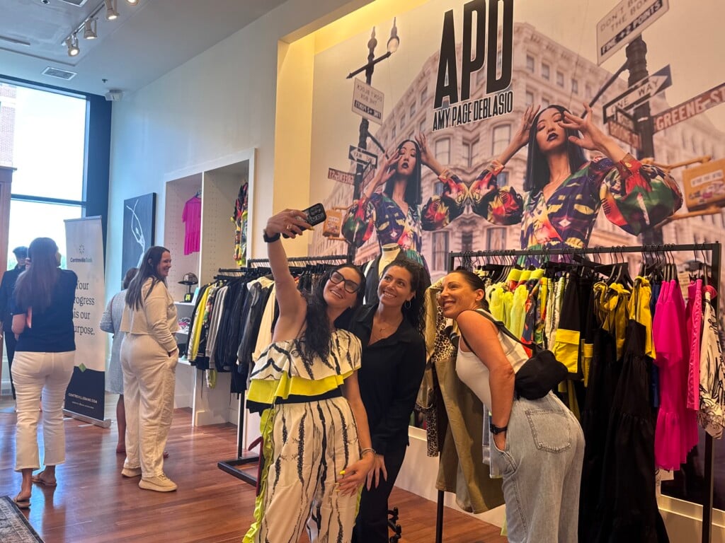 Three women take a selfie in front of a clothing display.