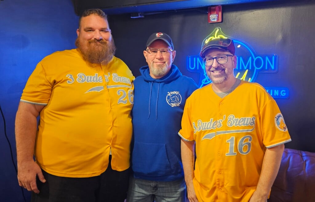 Three men wearing shirts that say "3 Dudes' Brews" pictured in a brewery.
