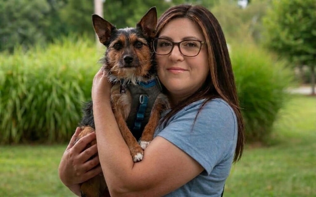 Sandra holds Tyson, a brown and black terrier mix, in a grassy outdoor setting.