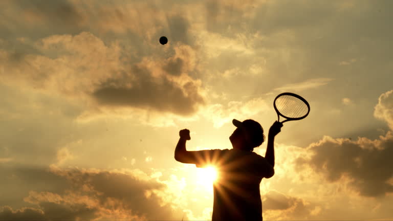 Silhouette Of Tennis Player Serving On Sunset Background.